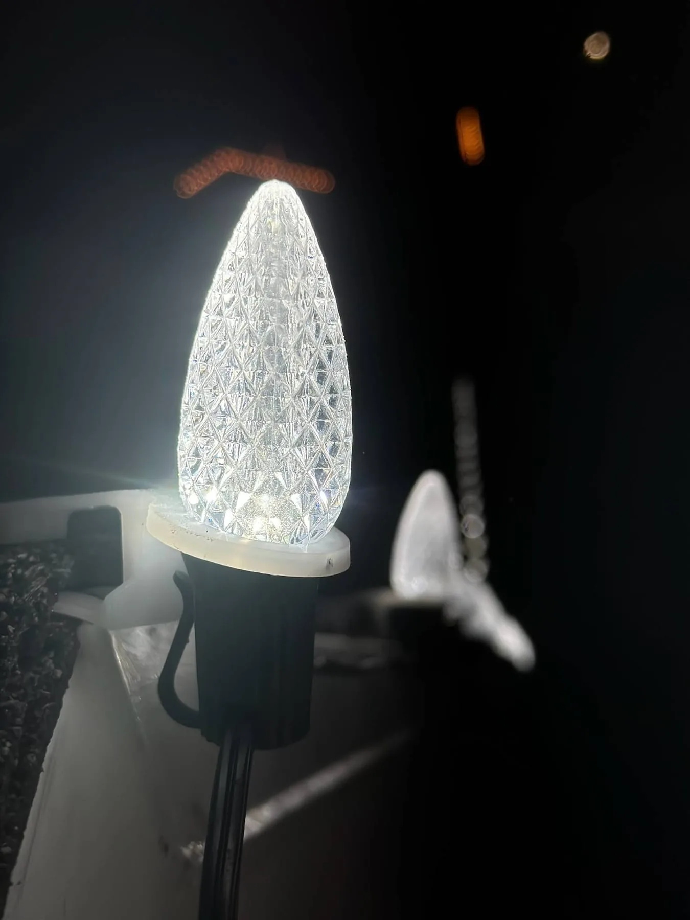 Close-up of a faceted C9 LED bulb clipped to a roofline