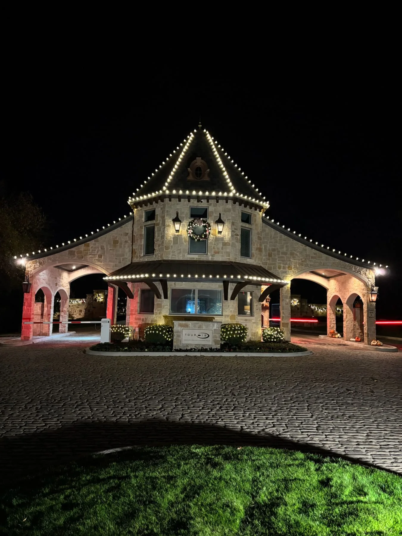 Warm white roofline lighting and a lit wreath on a gated-community entrance building