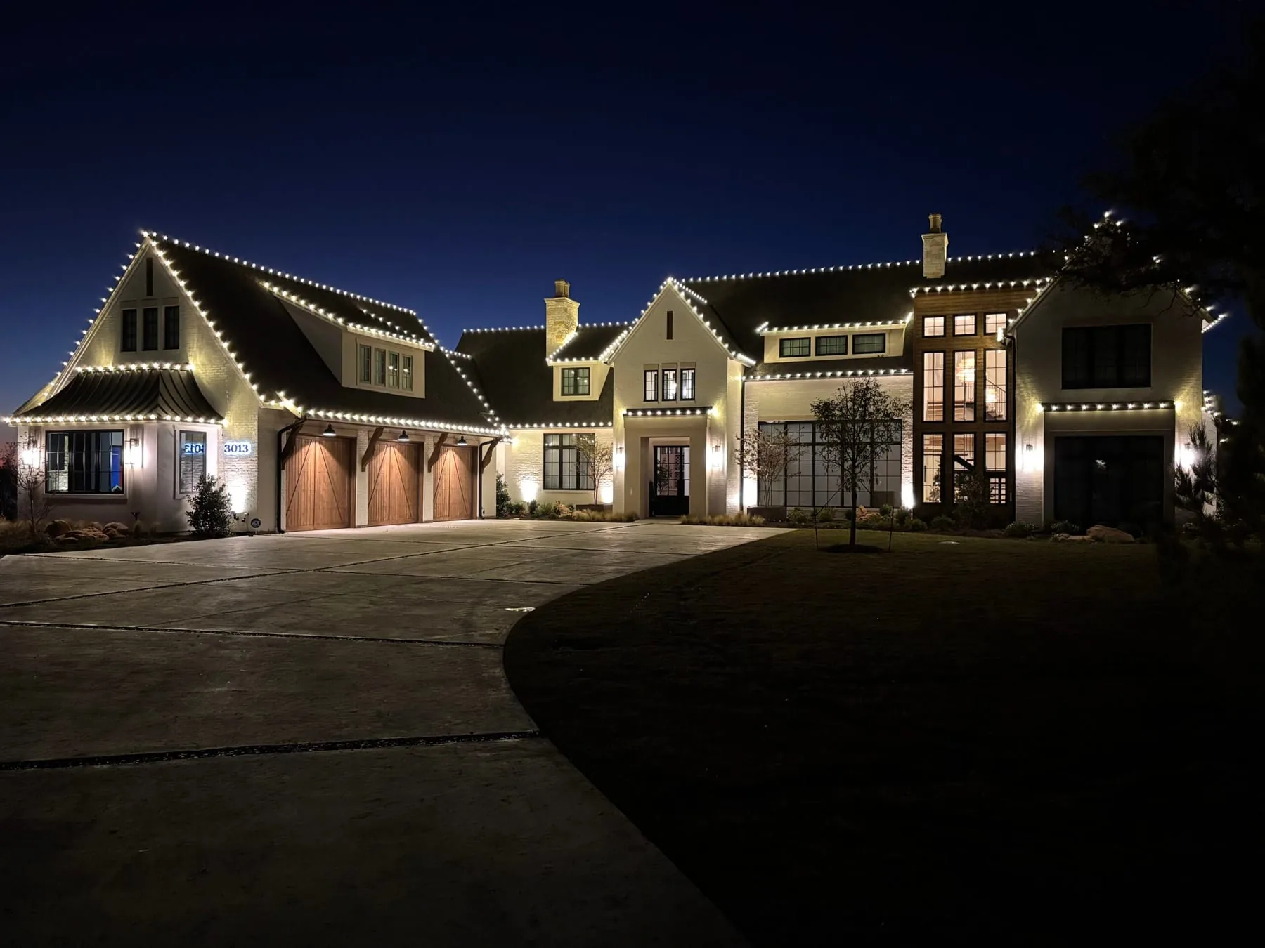 Warm white roofline lighting outlining a large home against a deep blue dusk sky