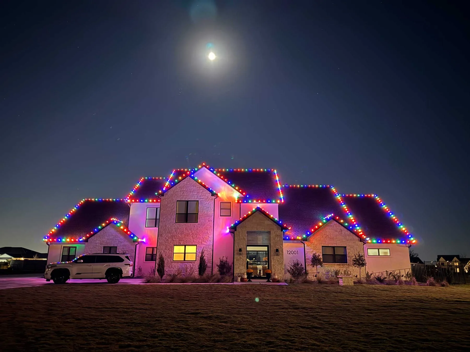 Multi-color roofline lighting on a two-story home under a full moon