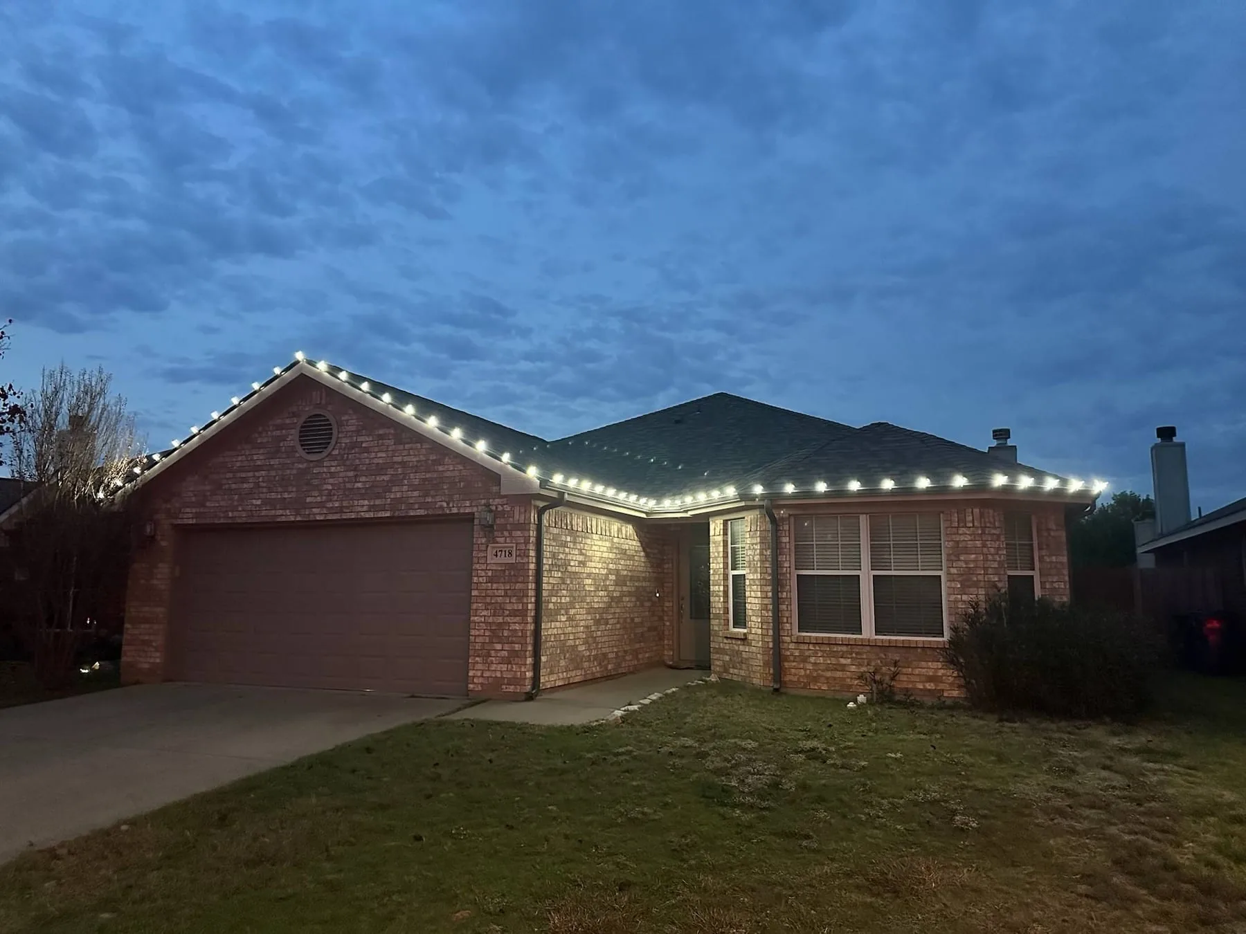 Warm white roofline lighting on a single-story brick home at dusk