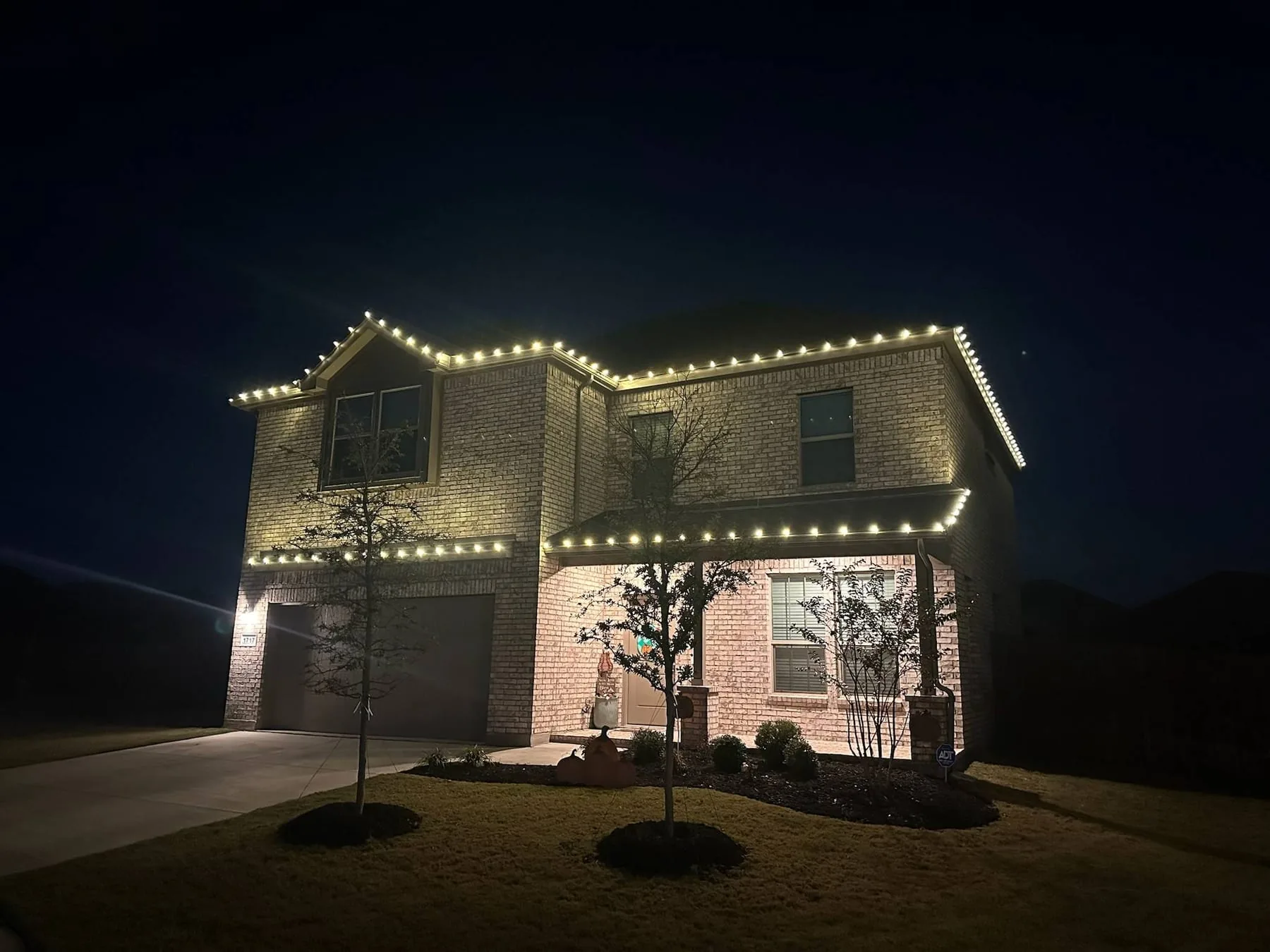 Warm white roofline lighting on a two-story brick home