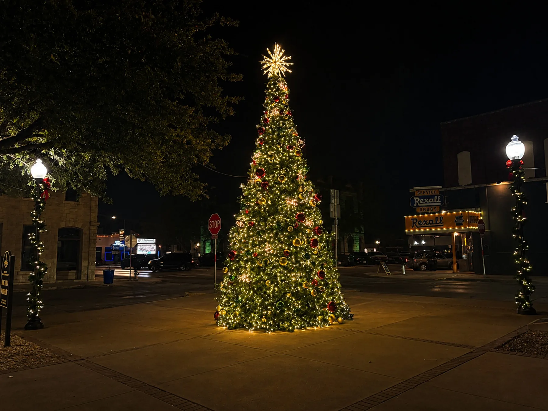 A large lit town square Christmas tree with garland-wrapped lamp posts