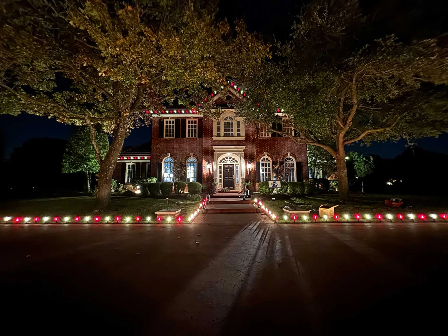 Red and white stake lights lining the walkway and drive of a brick home